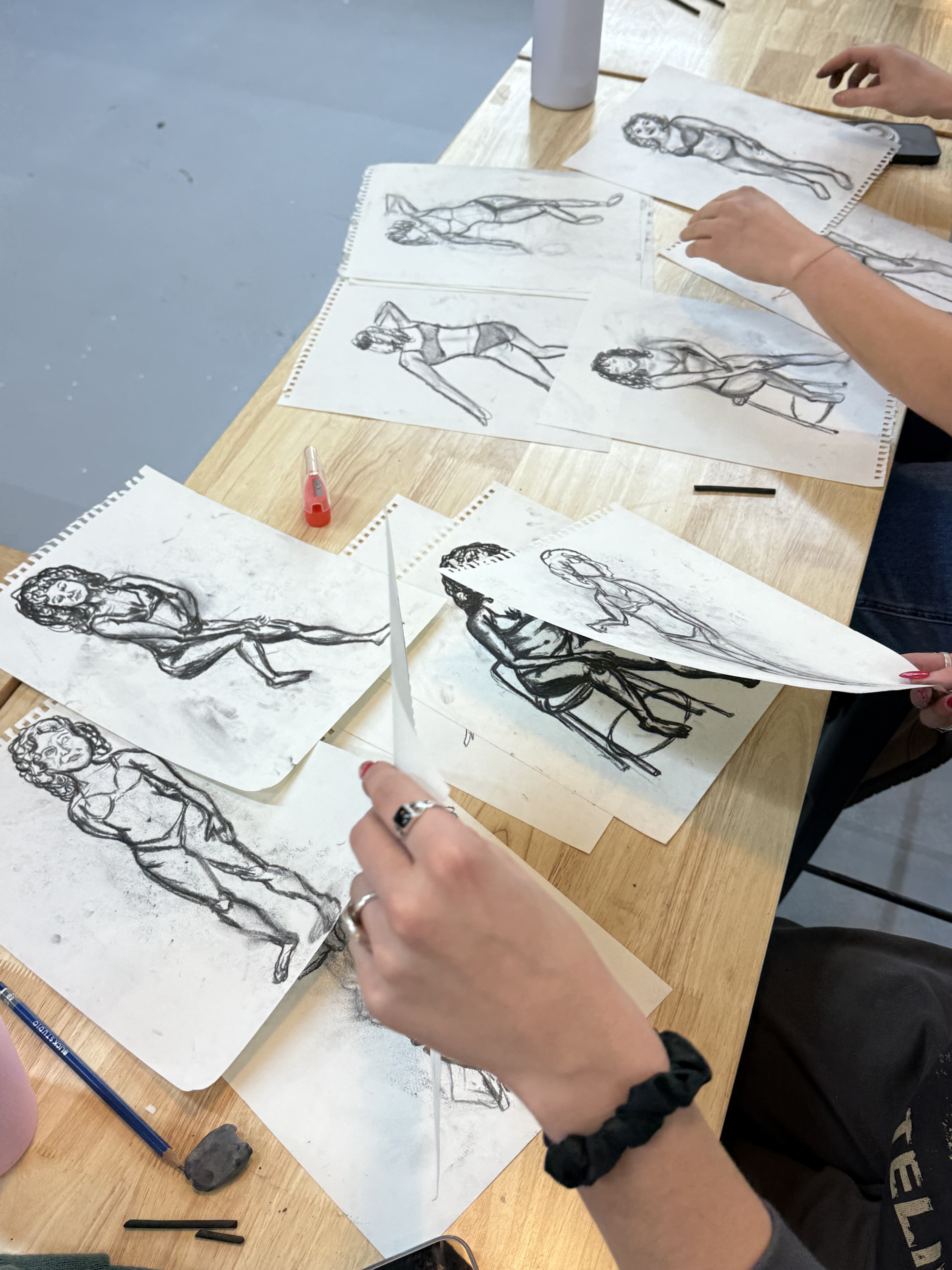 A spread of finished charcoal figure studies on a studio table