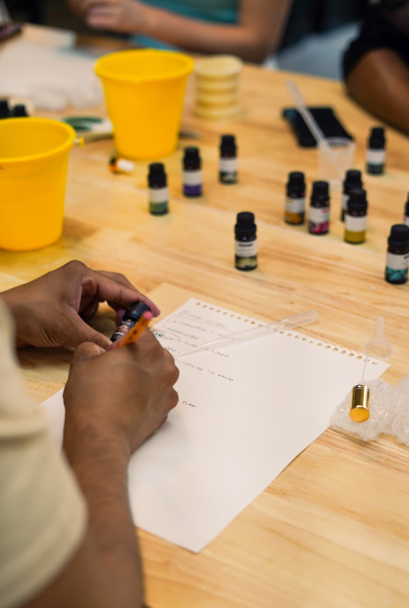 Guest writing down a formula on a blending worksheet beside fragrance bottles and a travel bottle
