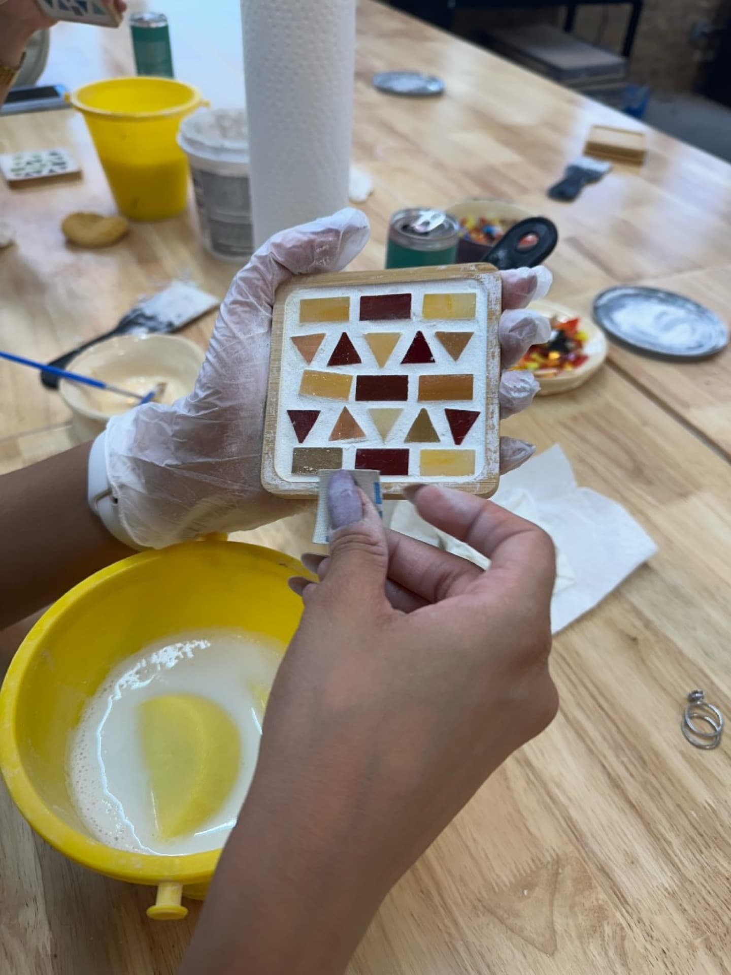 Hands grouting a colorful mosaic coaster
